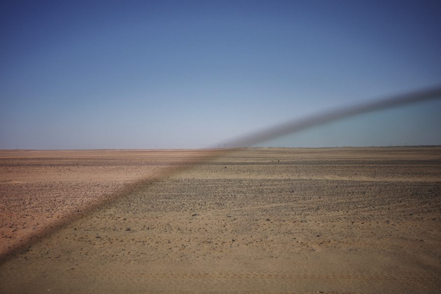 The vast desert horizon is viewed through the tinted window of a Mercedes-Benz. To survive the extreme temperatures, which can exceed 50°C (122°F), and the blinding light, drivers heavily tint their windows as they navigate the tracks connecting the widely scattered camps.
