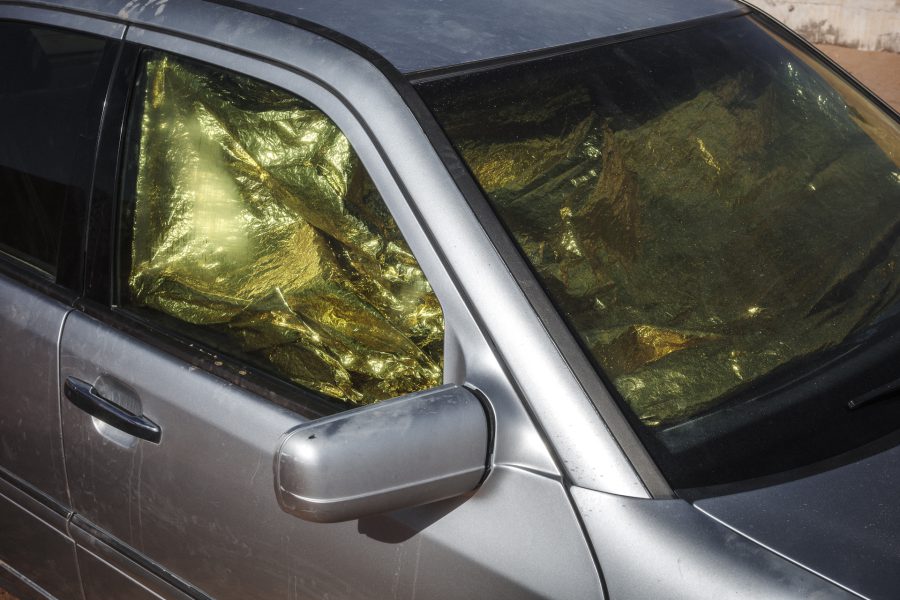 A gold thermal emergency blanket is used as a makeshift sunshade in the window of a Mercedes-Benz. Owners in the camps use creative and low-cost methods to protect the interiors of their vehicles from the sun, preserving the cars that are essential for their survival.